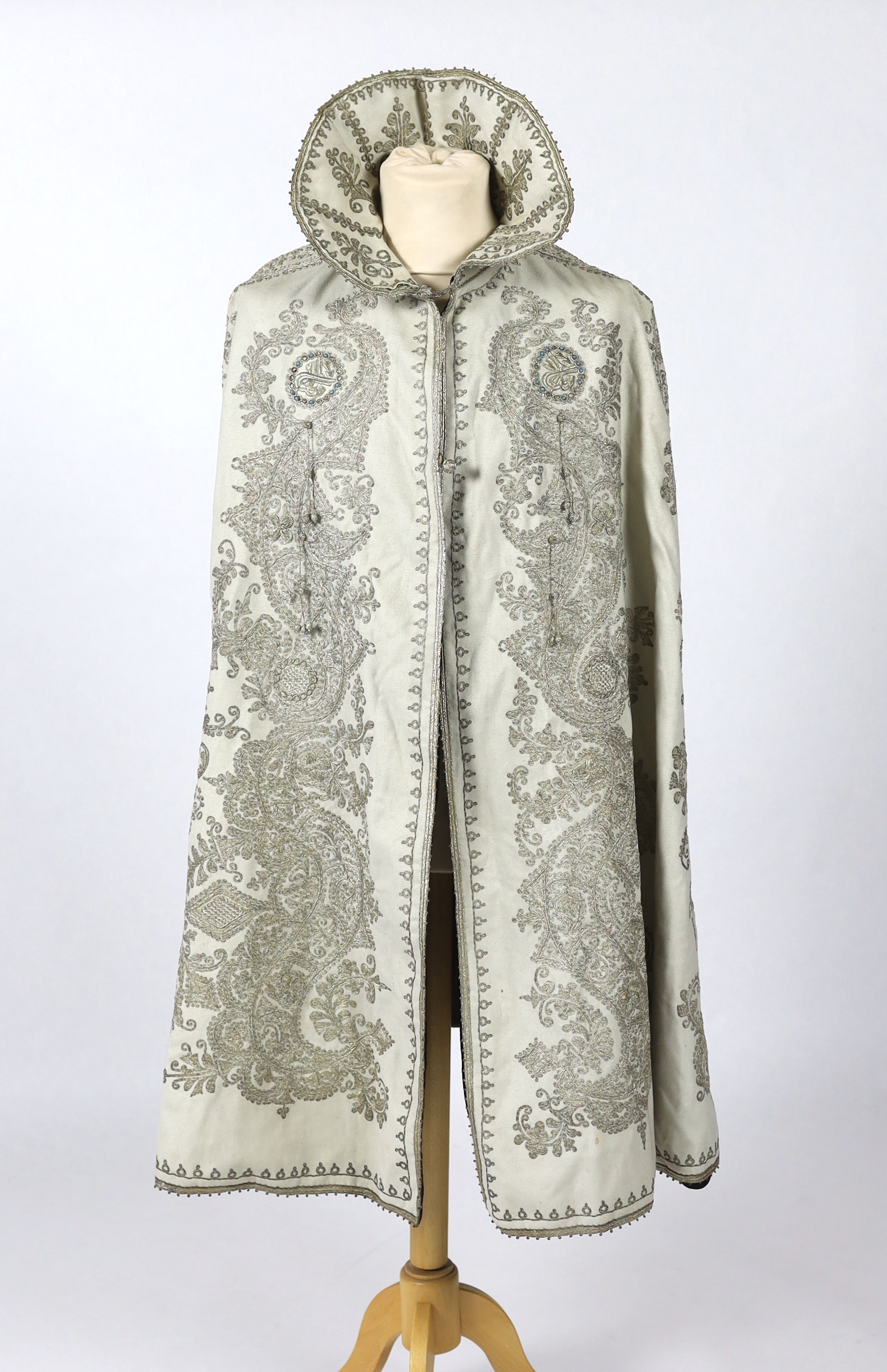 A 19th century Indian fine cream wool embroidered cape, probably made for the European market, embroidered in panels of silver metallic thread in an ornate vertical design with turquoise embellishments and lined in black